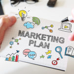 Mans hand drawing Marketing Plan concept on white notebook