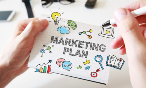 Mans hand drawing Marketing Plan concept on white notebook