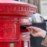 Throwing a letter in a red British post box from the side