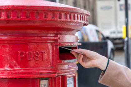 Throwing a letter in a red British post box from the side